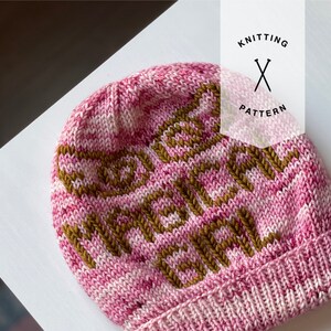 May include: Pink and white knitted hat with a brown knitted pattern that says "Make it a French Thing".