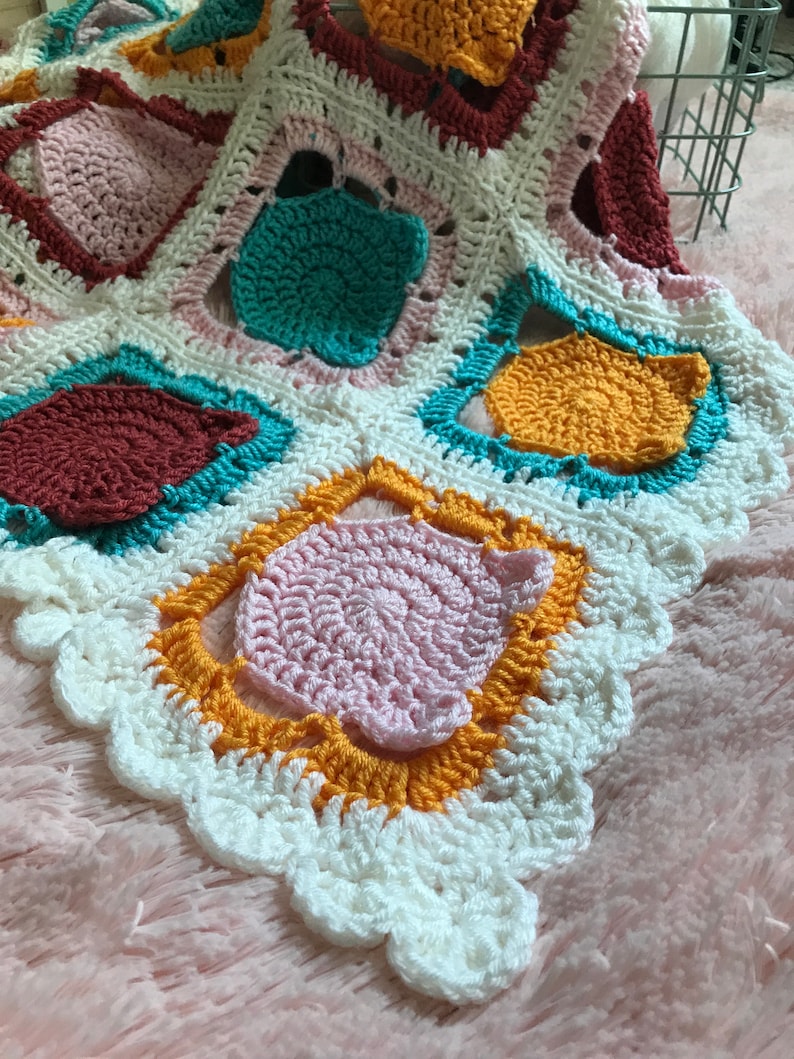 May include: A crocheted blanket with a white background and colorful squares in shades of pink, yellow, orange, teal, and burgundy. The blanket has a scalloped edge.