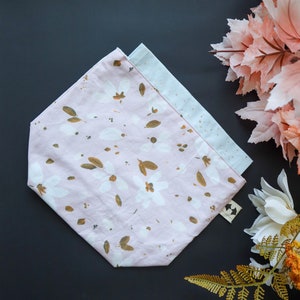 May include: A pink fabric pouch with a floral pattern in shades of brown and white. The pouch is folded in half and has a small tag attached to it.
