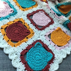 May include: A crocheted blanket with a white background and colorful squares. The squares are made of different colors of yarn, including teal, pink, brown, and yellow.