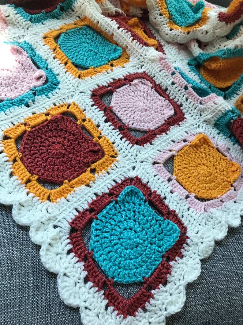 May include: A crocheted blanket with a white background and colorful squares. The squares are made of different colors of yarn, including teal, pink, brown, and yellow.