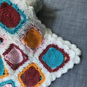 May include: A white crocheted blanket with a scalloped edge. The blanket is made up of squares with different colored circles in the center. The colors of the circles are red, orange, pink, and blue.