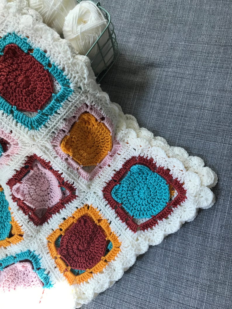 May include: A white crocheted blanket with a scalloped edge. The blanket is made up of squares with different colored circles in the center. The colors of the circles are red, orange, pink, and blue.
