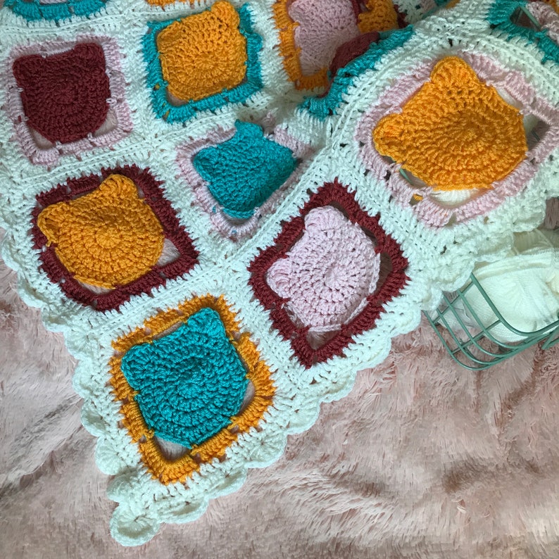 May include: A crocheted blanket with a white background and colorful squares. The squares are made of different colors of yarn, including yellow, pink, blue, and brown. The blanket has a scalloped edge.