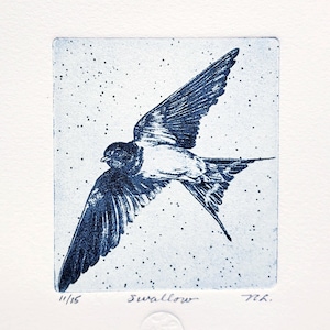 May include: A blue and white print of a swallow in flight. The bird is depicted with outstretched wings against a speckled background. The word "Swallow" is written below the image, along with the edition number 11/15.
