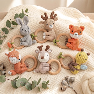 May include: A selection of handmade crochet baby rattles shaped like animals, such as a rabbit, deer, fox, and bee. Each rattle has a wooden ring and is made in colours like grey, orange, and brown. These rattles are designed for infants and babies.