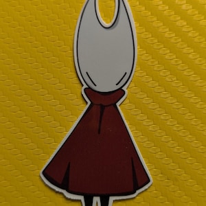 May include: A sticker depicting a character with a white head and a maroon cape. The character has a simple design with a black outline, set against a yellow background.