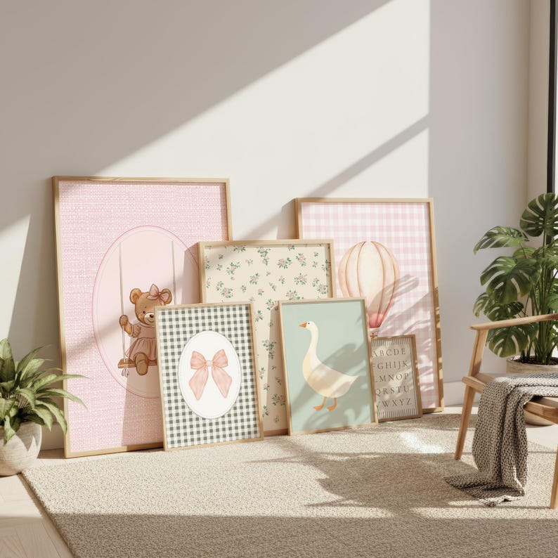 May include: A selection of framed art prints with a soft colour palette. The prints depict a teddy bear, a bow, a goose, and a hot air balloon. The frames are light wood. The prints have pink, green, and beige tones.