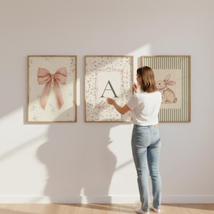 May include: Three framed art prints with a floral and bunny theme. One print features a pink bow, another has the letter "A", and the third shows a bunny with a pink bow. The prints are in wooden frames.