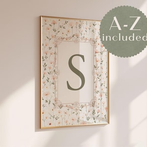 May include: A framed floral print with the letter "S" in green. The artwork is in a gold frame, with a floral pattern and the text "A-Z included" in a circular design. The print is a decorative piece.