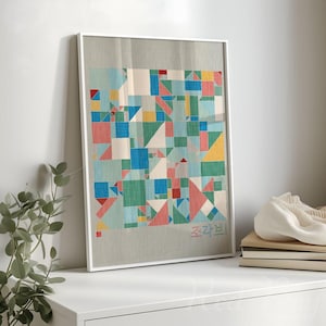 May include: A framed artwork featuring a colorful patchwork design with geometric shapes in shades of blue, green, red, and yellow. The artwork is displayed on a white surface, with the Korean text "Jogakbo" visible. The frame is white.