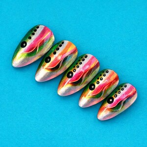 May include: Five iridescent nail art designs with a rainbow color scheme, featuring a silver base, green, pink, and orange stripes, and black dot accents. The nails are almond-shaped and arranged on a bright blue background.