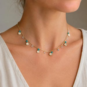 May include: A gold chain necklace featuring evenly spaced dangling charms, including small ridged gold shells and alternating round beads in bright turquoise and translucent clear glass, secured with a delicate link chain design.