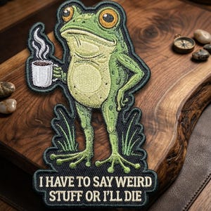 May include: Embroidered patch featuring a green frog holding a coffee cup. The frog has large yellow eyes and is standing with one hand on its hip. The patch includes the text, "I HAVE TO SAY WEIRD STUFF OR I'LL DIE."