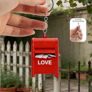 May include: A red mailbox keychain with the word "LOVE" in white. The keychain is made of 2D flat acrylic and has a thickness of 0.15 inches. The mailbox is filled with white paper and hangs from a silver chain.