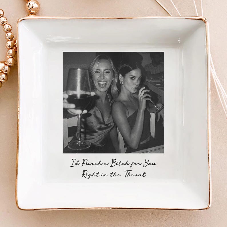 May include: White square ceramic trinket dish with gold trim. The center features a black and white photo of two women drinking wine. The text "I'd Punch a Bitch for You Right in the Throat" is printed below the photo.