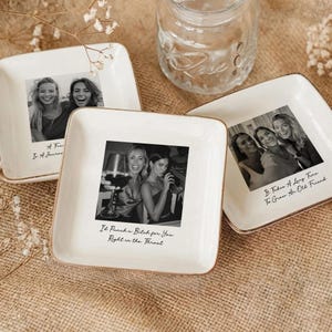 May include: Set of three square, white ceramic dishes with gold rims. Each dish features a black and white photograph of smiling women. Text on the dishes reads: "A F I A Journe", "It'd Punch a Bitch for You Right in the Throat", and "It Takes A Long Time To Grow An Old Friend."