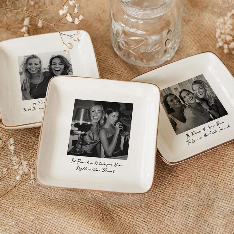 May include: Set of three square, white ceramic dishes with gold rims. Each dish features a black and white photograph of smiling women. Text on the dishes reads: "A F I A Journe", "It'd Punch a Bitch for You Right in the Throat", and "It Takes A Long Time To Grow An Old Friend."