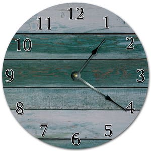 Peut inclure: Horloge murale ronde avec un cadran effet bois vieilli. Le cadran présente des planches horizontales dans des tons de turquoise, de bleu et de blanc. Des chiffres noirs indiquent les heures, et des aiguilles noires indiquent l'heure. Design simple et moderne.