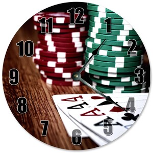 May include: Round wall clock with a poker theme. The clock face features a wooden background, stacks of red and green poker chips, and playing cards. The clock hands point to the time, with the numbers 1 through 12 around the clock face.