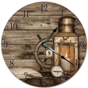 Peut inclure: Horloge murale ronde sur le thème nautique. Le cadran de l'horloge présente un fond en bois avec un gouvernail, une lanterne avec une bougie allumée, une boussole et un livre ouvert. Les aiguilles de l'horloge sont noires.