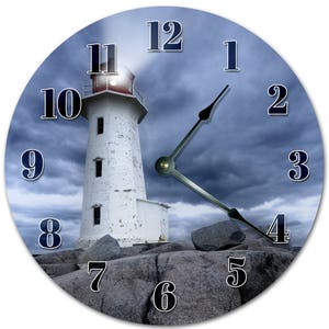 May include: Round wall clock featuring a white lighthouse with a red top, set against a stormy sky. The clock face displays black numerals and hands, resting on a rocky shoreline. The clock's design evokes a nautical theme.