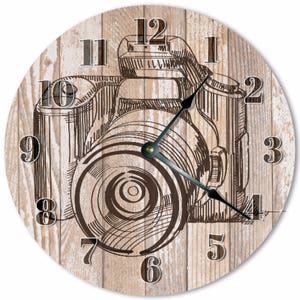 May include: Round wall clock with a vintage camera design. The clock face features a detailed sketch of a camera in brown tones against a light wood grain background. Black clock hands and white numerals complete the design.