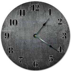May include: A round wall clock with a distressed gray background and black numerals. The clock hands are black and the clock face has a scratched appearance. The numbers are in a bold, sans-serif font.