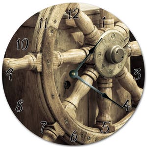 Peut inclure: Horloge ronde en bois avec un design de roue de navire. Le cadran de l'horloge comporte des chiffres noirs et des aiguilles noires. L'horloge est en bois brun clair et a un thème nautique vintage.
