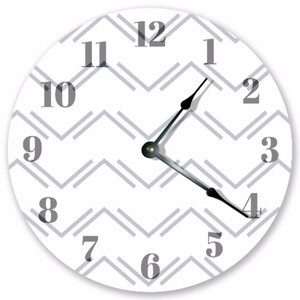 May include: A round wall clock with a white face and a gray chevron pattern. The clock features black hands and gray numerals. The hands point to 1:20. A decorative piece for any room.