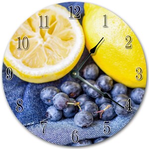 May include: A clock face with a blue denim background, two lemons, and blueberries. The numbers 1 through 12 are displayed around the clock face.