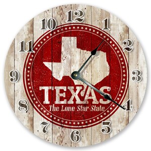 May include: Round wall clock with a rustic wood grain background. The clock face features a red Texas state outline and the word "TEXAS" in white. The text "The Lone Star State" is below the word Texas. Black clock hands.