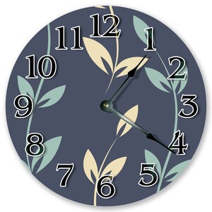 May include: Round wall clock with a navy blue face featuring a floral pattern in light green and beige. The clock hands are black, and the numbers are white with a black outline. The clock is a decorative item.