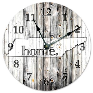 May include: Circular wall clock with a weathered wood effect. The clock face displays the white outline of Tennessee, with the word "home" in black. Black clock hands and numerals are set against the wood grain.