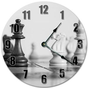 May include: Black and white clock with chess pieces on a chessboard. The clock face has black numbers on a white background. The chess pieces are in the foreground, with the black queen in the lower left corner and the white knight in the center.