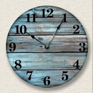 May include: Round wall clock with a distressed blue and gray wood grain design. The clock face features black numerals and hands, with a simple, classic aesthetic. A decorative piece for any room.