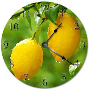 May include: Round wall clock featuring a vibrant image of two ripe yellow lemons on a branch with green leaves. The clock face displays black numerals and black clock hands against a green background.