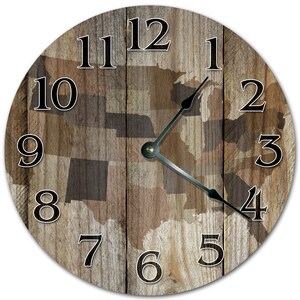May include: Round wall clock with a wooden background featuring the outlines of U.S. states. The clock face has black numerals and hands, with a brass-coloured centre. The clock's design incorporates a rustic aesthetic.