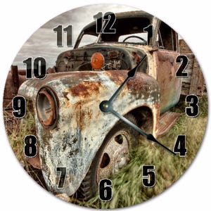 Peut inclure: Horloge murale ronde représentant un vieux camion rouillé. Le cadran affiche des chiffres noirs sur l'image du véhicule usé. Les aiguilles de l'horloge indiquent environ 16h18. Le camion est dans un champ herbeux sous un ciel nuageux.