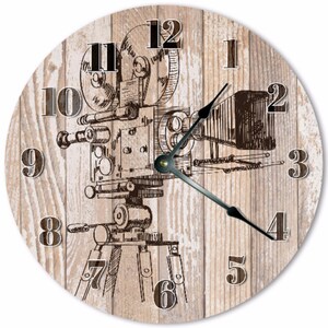 Peut inclure: Horloge murale ronde avec une illustration marron d'une caméra de cinéma vintage sur un fond clair en bois. Le cadran de l'horloge présente des aiguilles noires et des chiffres clairs. Un élément décoratif pour la maison ou le bureau.