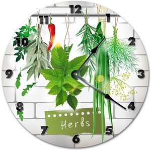 May include: Round wall clock featuring a white brick background and a collection of fresh herbs. The clock face displays a variety of green herbs, a red chili pepper, and the word "Herbs" on a green label. Black clock hands indicate the time.