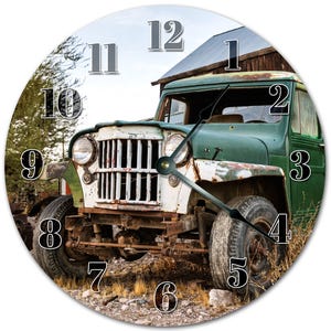 Peut inclure: Horloge murale ronde représentant une Jeep verte et blanche vintage. Le cadran affiche de grands chiffres et des aiguilles faciles à lire. L'arrière-plan montre la Jeep garée près d'une structure en bois vieillie, évoquant un thème rustique et extérieur.