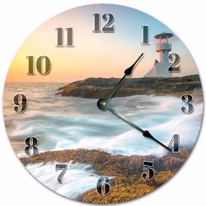 May include: Circular wall clock depicting a coastal scene with a lighthouse. The clock face has large numerals and black hands. The background shows a sunset over the ocean, with waves and a lighthouse. The clock is a decorative item.