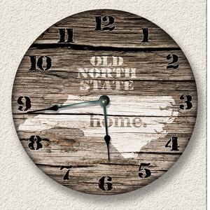 May include: Round wooden wall clock with a rustic design. The clock face features a distressed wood texture, black numerals, and the words "OLD NORTH STATE home." The clock hands are black.