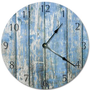 Peut inclure: Horloge murale ronde avec un motif de grain de bois bleu et blanc vieilli. Le cadran de l'horloge comporte des chiffres noirs et des aiguilles noires. Le design de l'horloge évoque une esthétique rustique et champêtre.