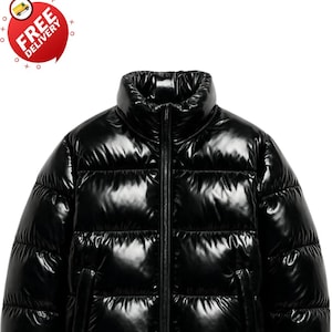 May include: A shiny black puffer jacket with a high collar and a full-length zip. The jacket features two side pockets and a ribbed hem and cuffs. The image also includes a "Free Delivery" graphic.