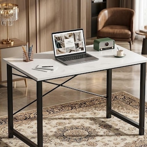 May include: A modern white desk with black metal legs. A laptop displaying a website, a green radio, and a cup of coffee sit on the desk. A gold lamp and a pencil holder are also visible. The desk is placed on a patterned rug.