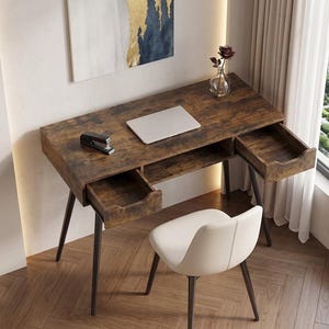 May include: A brown wooden desk with two drawers, a laptop, and a stapler. The desk has a distressed finish and sits on black metal legs. A white chair is positioned in front of the desk. A painting hangs on the wall above the desk.