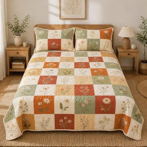 May include: A floral quilt and two matching pillow shams. The quilt features a patchwork design with squares of cream, orange, green, and rust, each adorned with embroidered flowers. The bedding is on a wooden bed frame, creating a cozy, inviting bedroom scene.
