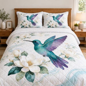 May include: White quilted bedding set featuring a large teal and purple hummingbird with outstretched wings, surrounded by white magnolia flowers and green leaves. Two matching pillowcases with hummingbird and flower designs.